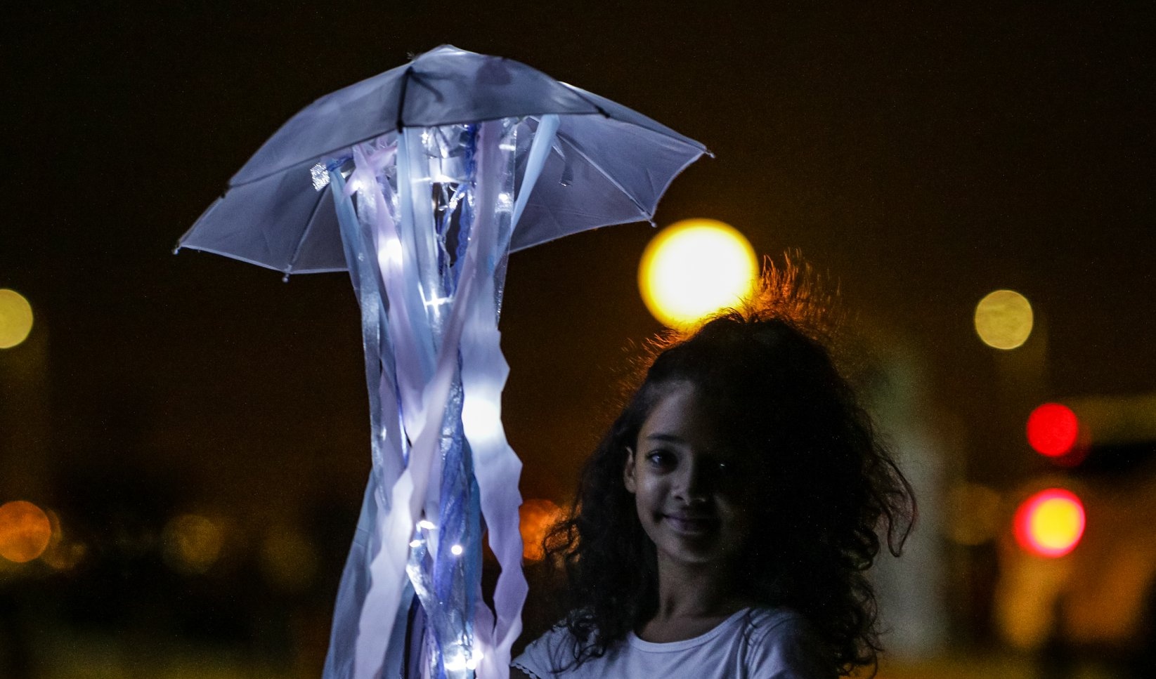 A young girl smiles beside a glowing jellyfish umbrella lantern at the lantern parade