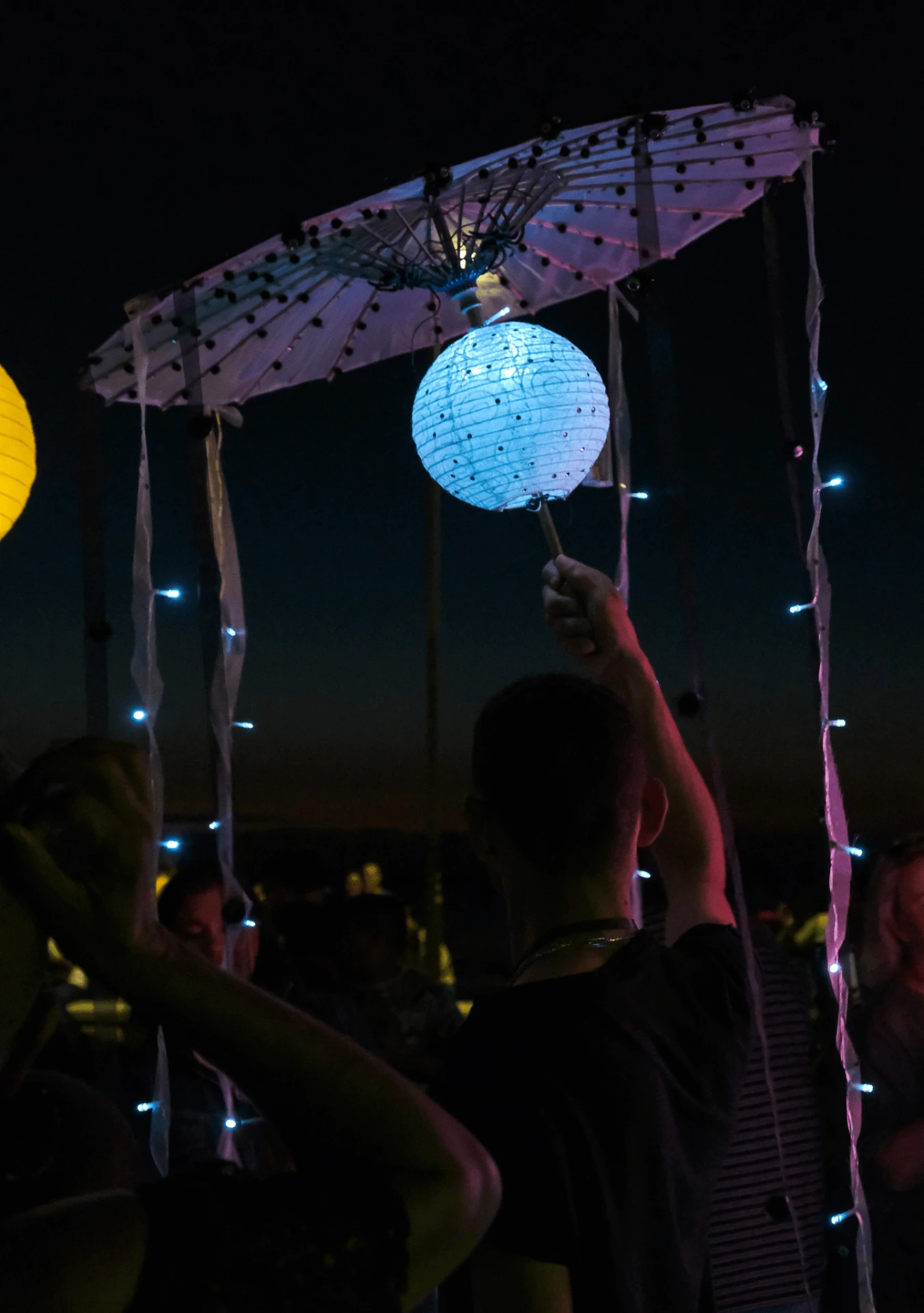 A glowing umbrella lantern with trailing lights held up against the night sky